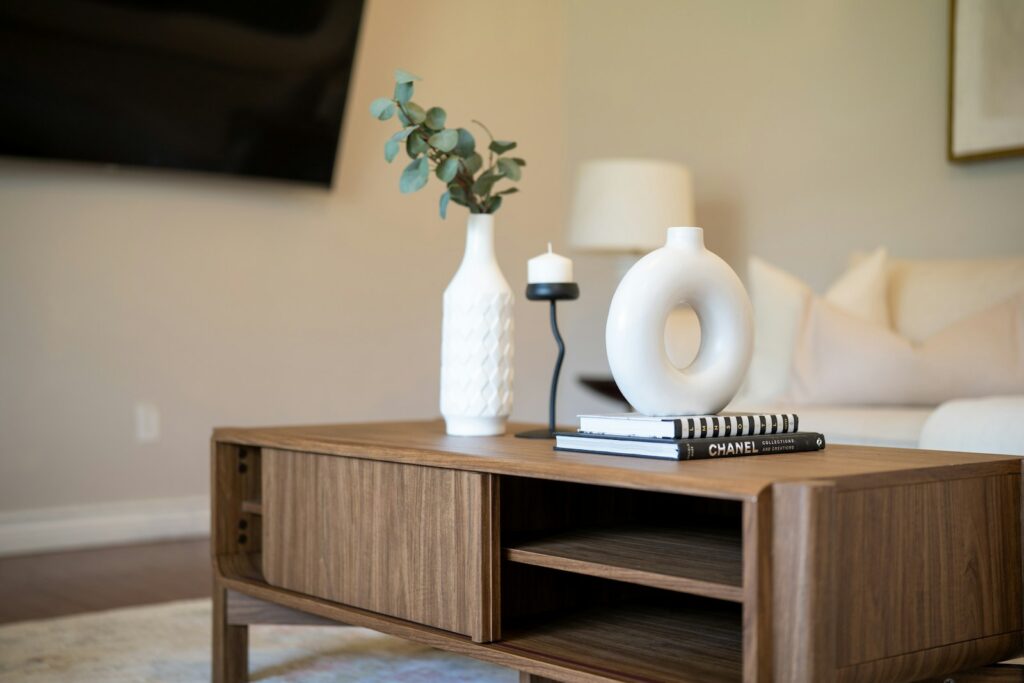 White sculptural vases and books arranged on a wooden table in a warm, neutral living room.