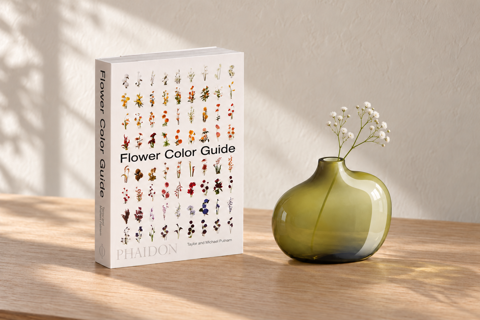 AI editorial illustration of a compact flower reference book beside a low green glass vase holding two delicate sprigs of white baby’s breath